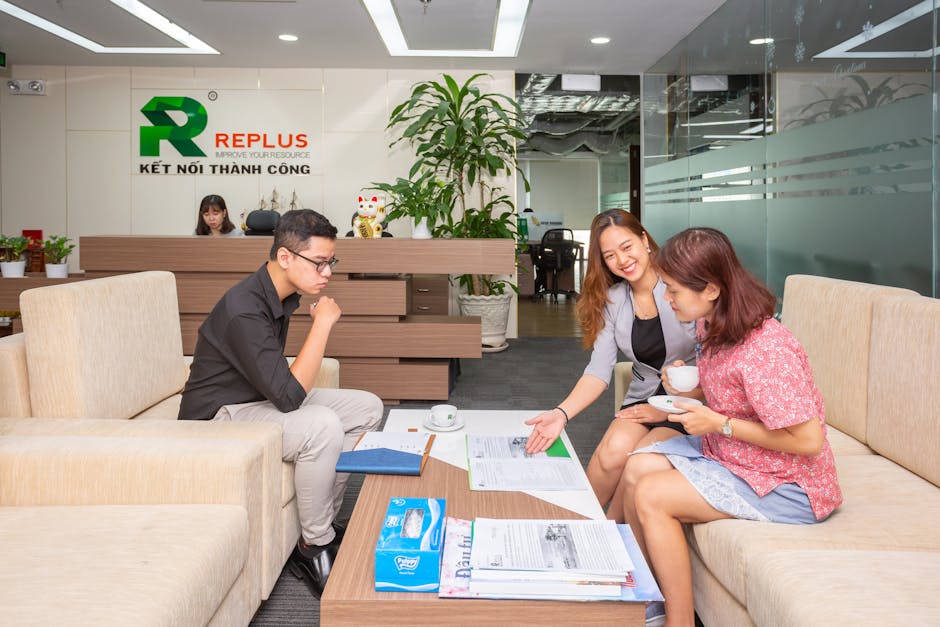 Group having a business meeting in a modern office with a receptionist in the background.