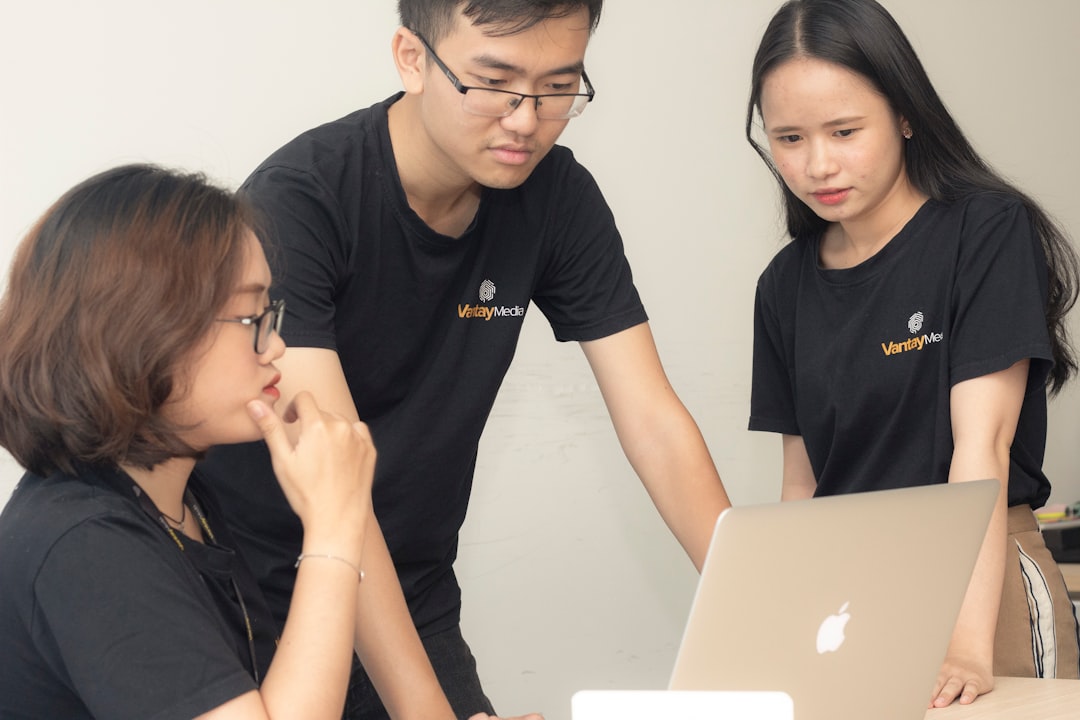 two women and one man looking onto MacBook screen