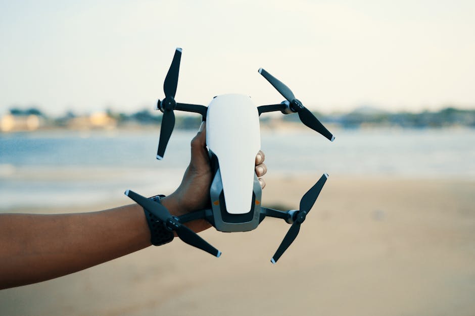 Close-up of a hand holding a drone on a beach during daytime, showcasing modern technology.