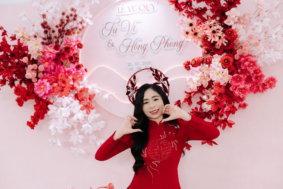 Asian woman in traditional dress poses amid vibrant floral decorations at a wedding event.