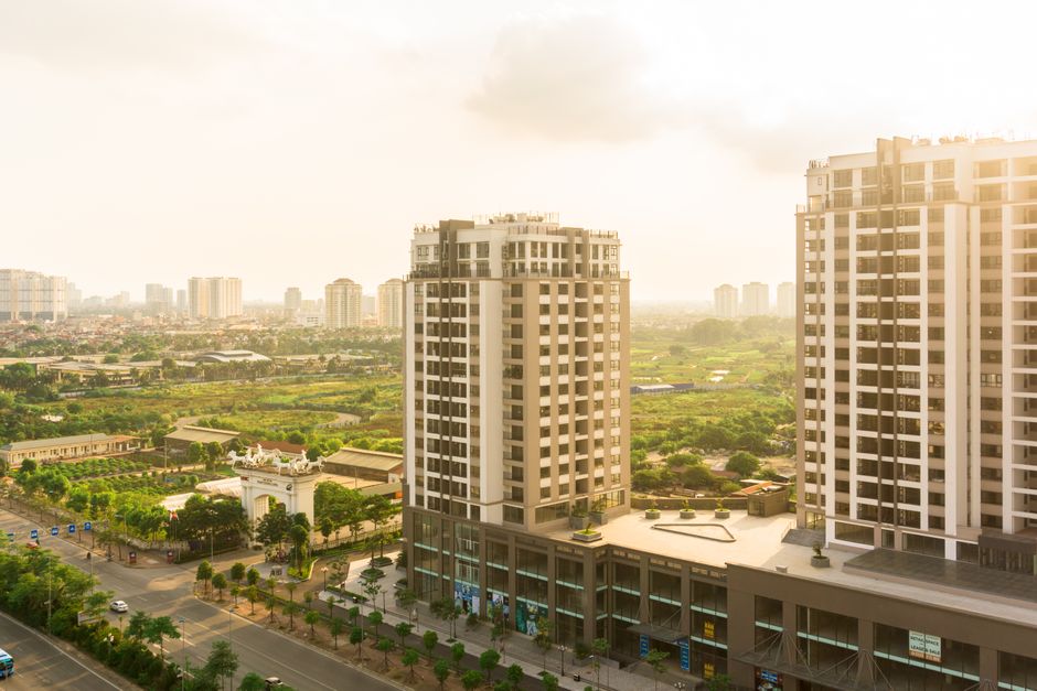 Elevated view of urban landscape with skyscrapers and green fields under sunlight.