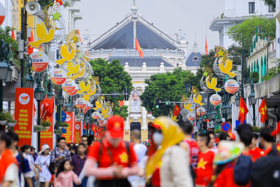 Vibrant street scene in Hanoi featuring people, flags, and the Hanoi Opera House.