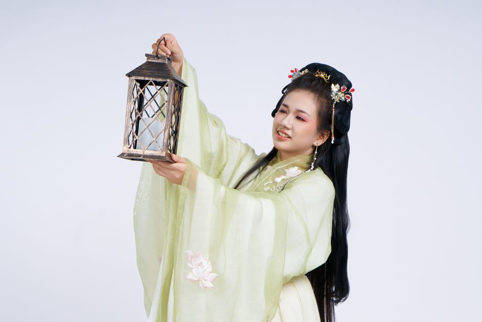 East Asian woman in traditional dress holding an antique lantern with a cheerful expression.