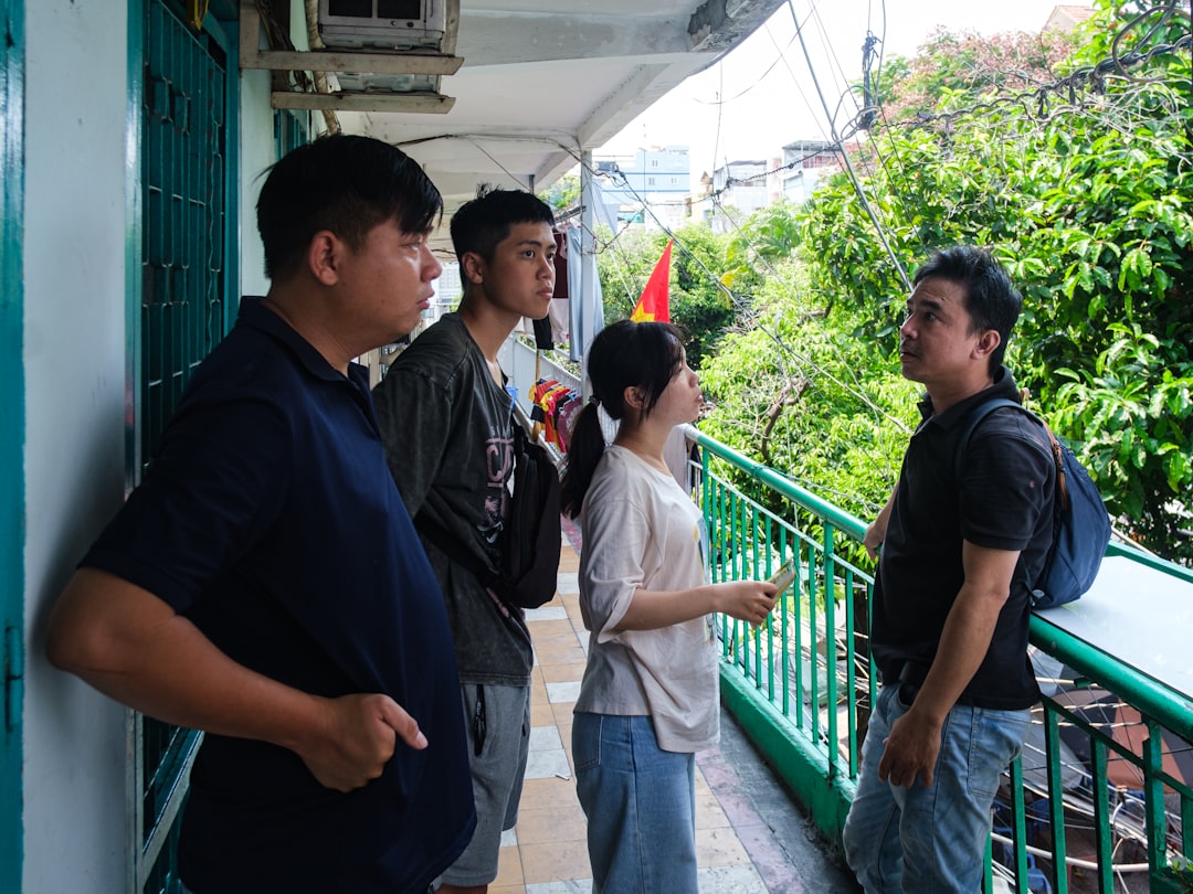 Four people converse on a green balcony overlooking trees.