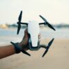 Close-up of a hand holding a drone on a beach during daytime, showcasing modern technology.