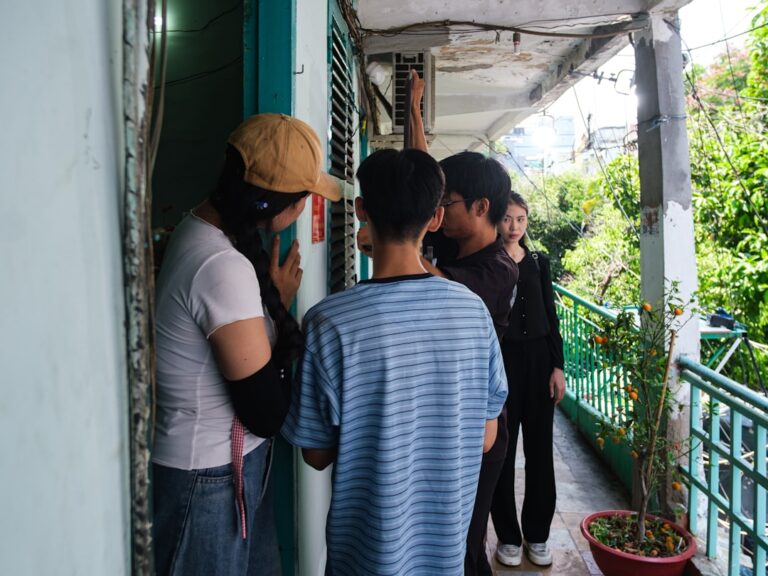 People talking on a narrow outdoor balcony with plants