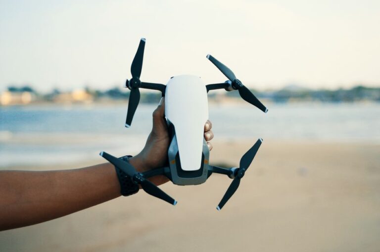 Close-up of a hand holding a drone on a beach during daytime, showcasing modern technology.