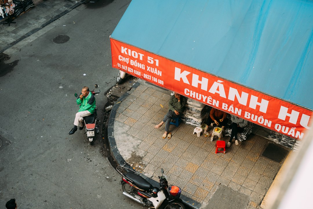 A person on a motorcycle beside people sitting on stools under a red awning